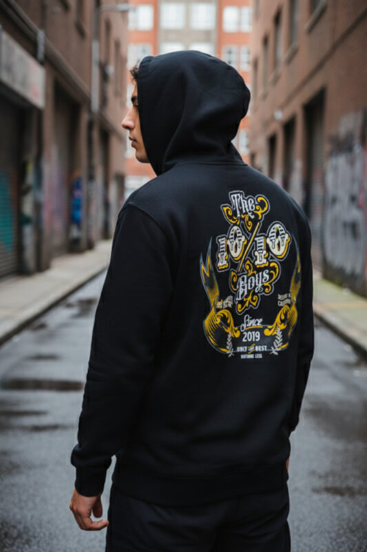 Model wearing a black hoodie in an urban alley, showing the back graphic and fit for The 10/10 Boys Sizing Guide.