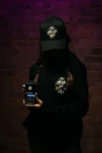 Model wearing The 10/10 Boys cap and hoodie holding a phone with the Telegram bot open