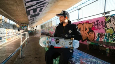 Marcos Baines for The 10/10 Boys skate collaboration wearing black streetwear and holding a skateboard