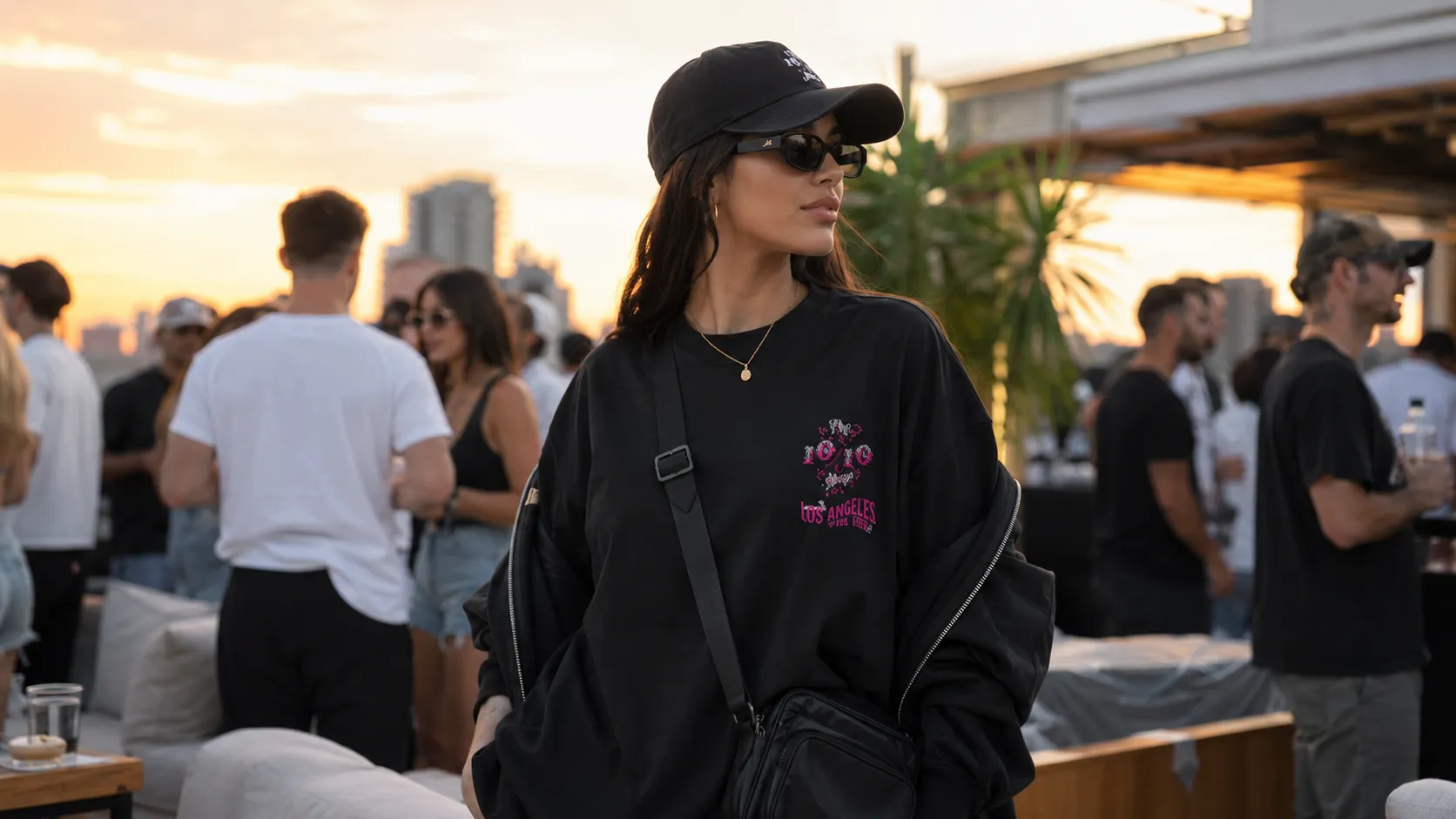 Night summer event outfit — lightweight black hoodie, structured cap, chain and crossbody bag at a rooftop event, golden hour