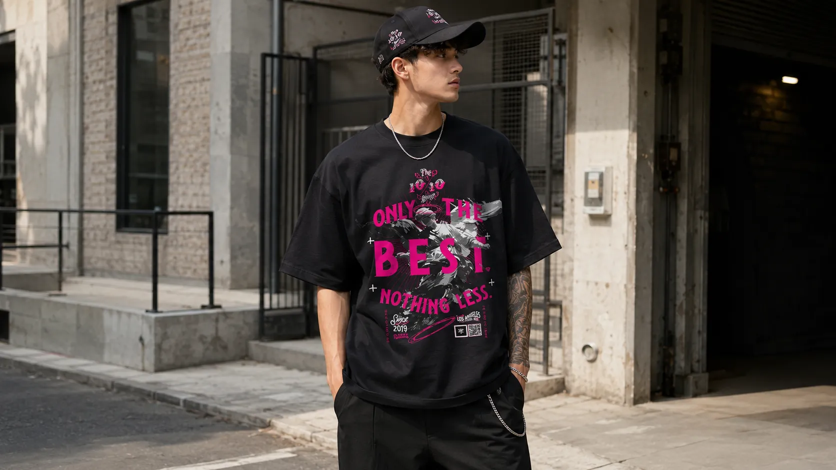 Black and pink streetwear outfit with a black graphic tee and black cap in an urban setting