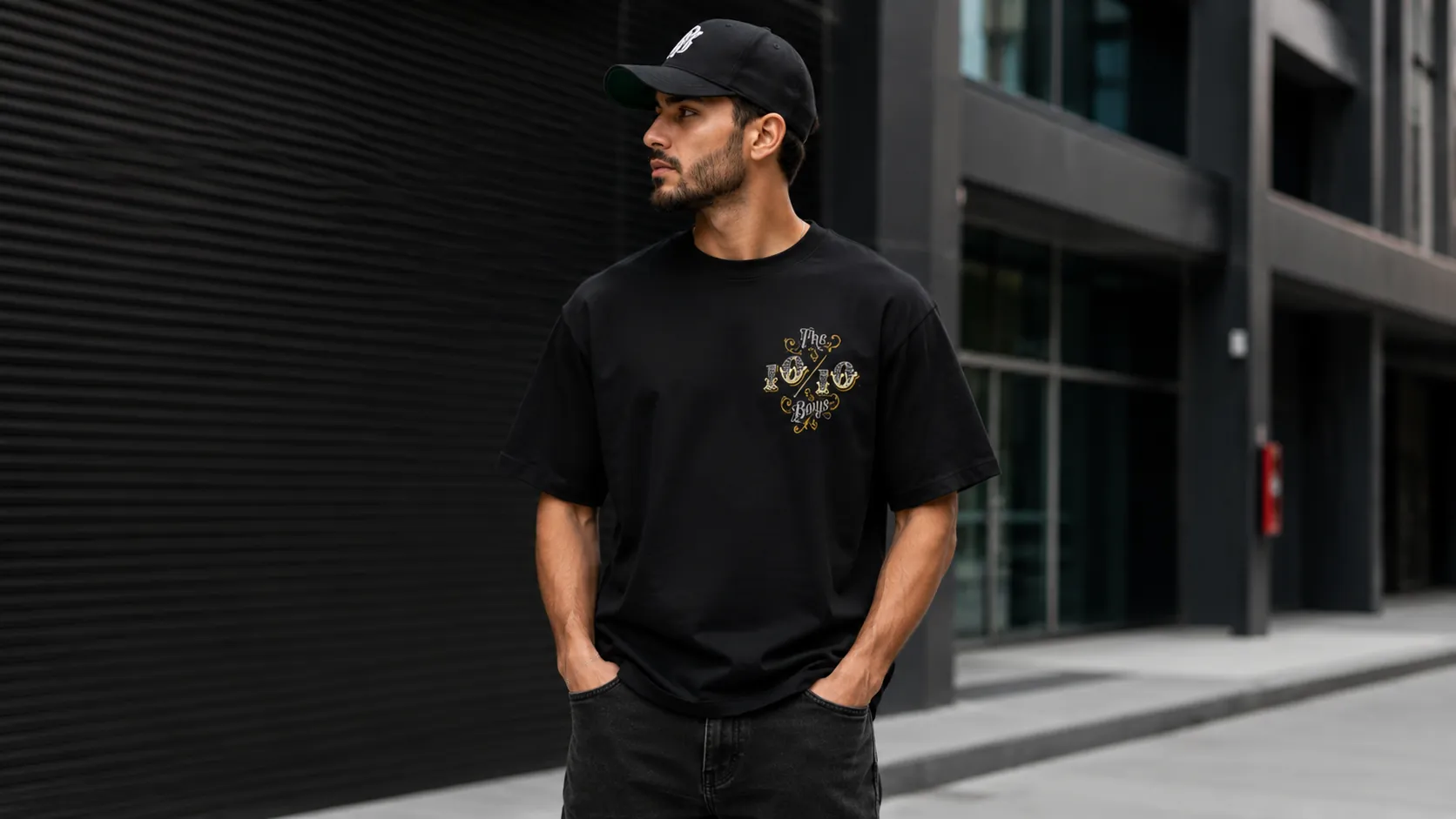 Minimal streetwear outfit: black tee, black cap and dark denim on a city street