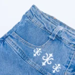 The 10/10 Boys denim skirt — close detail of the white fleur-de-lis print on light-wash denim