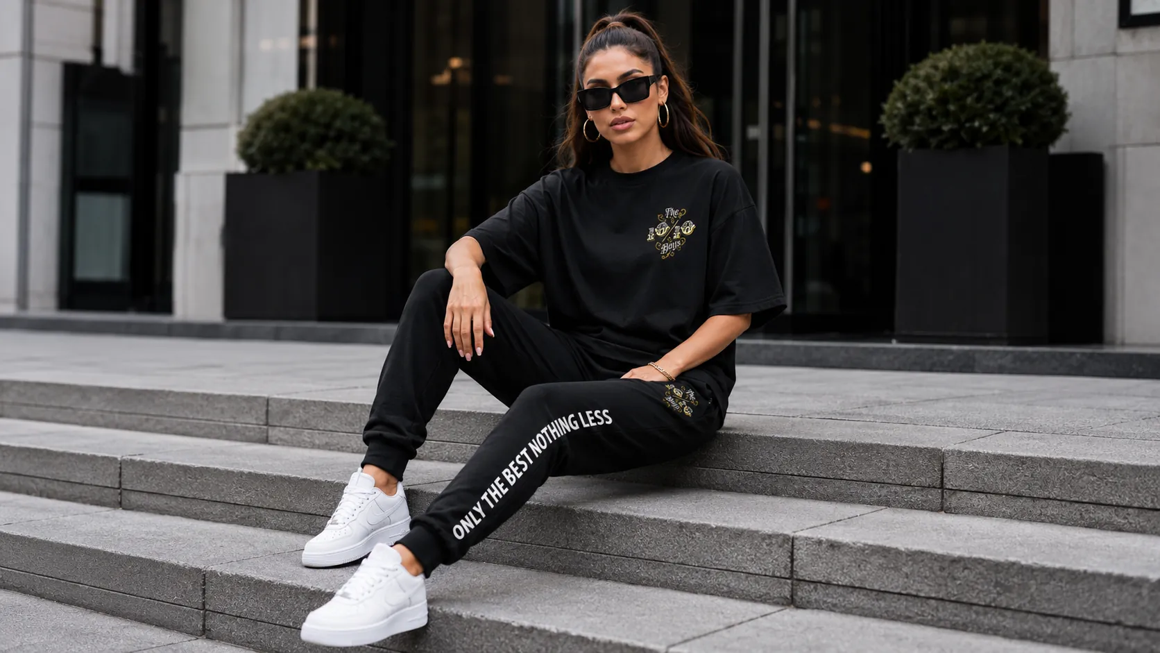 Seated on concrete steps in a black tee and joggers with a white side print