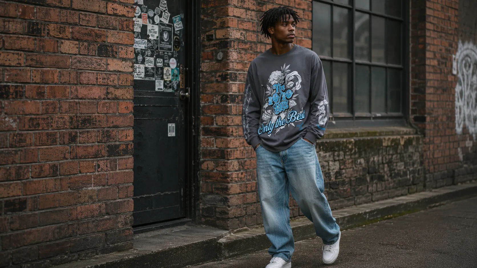 Full-length street shot of a charcoal graphic long sleeve tee worn with baggy light-wash jeans and white trainers