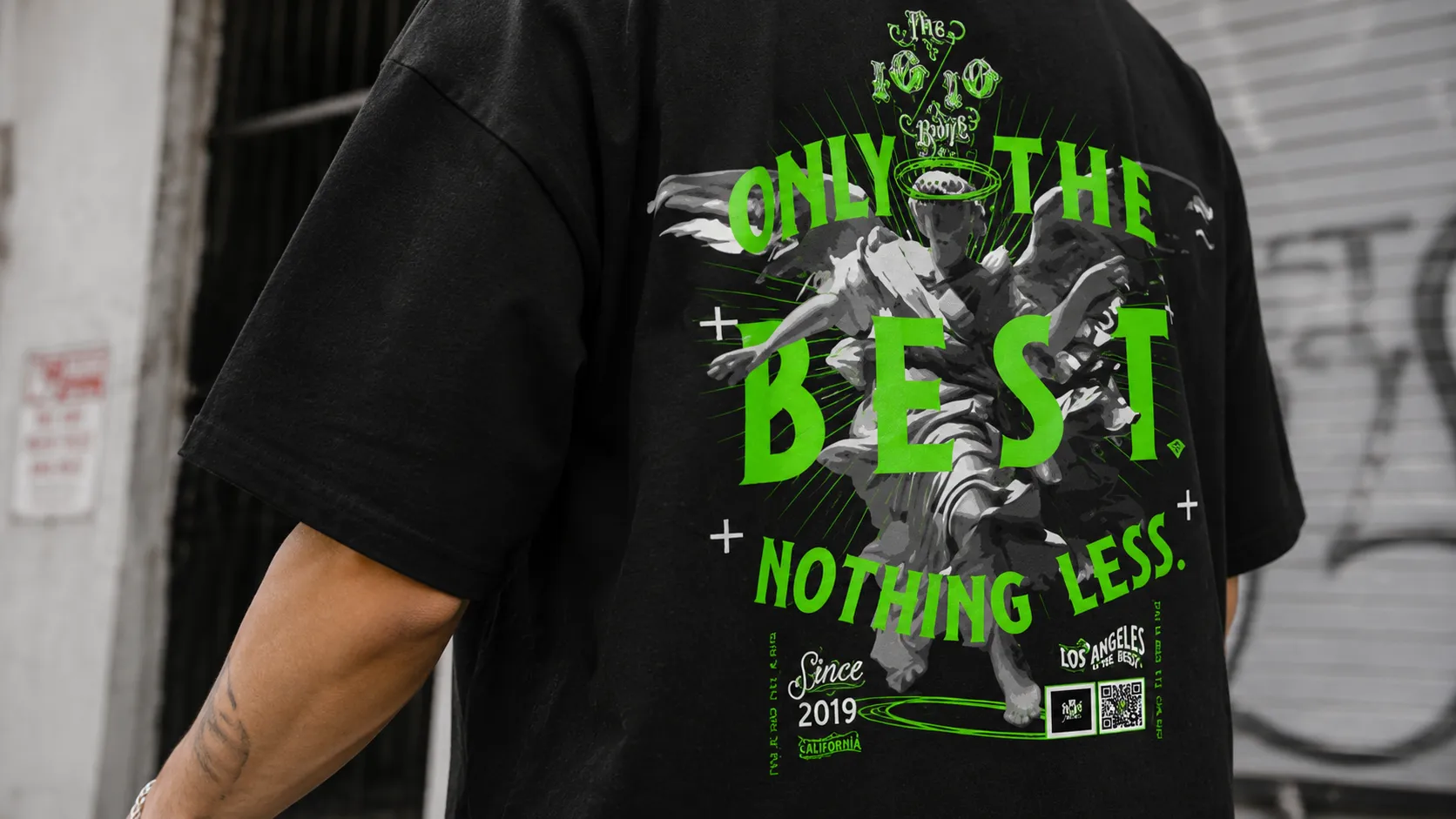 Back view of a black tee showing the green Only The Best Nothing Less graphic against a graffiti shutter