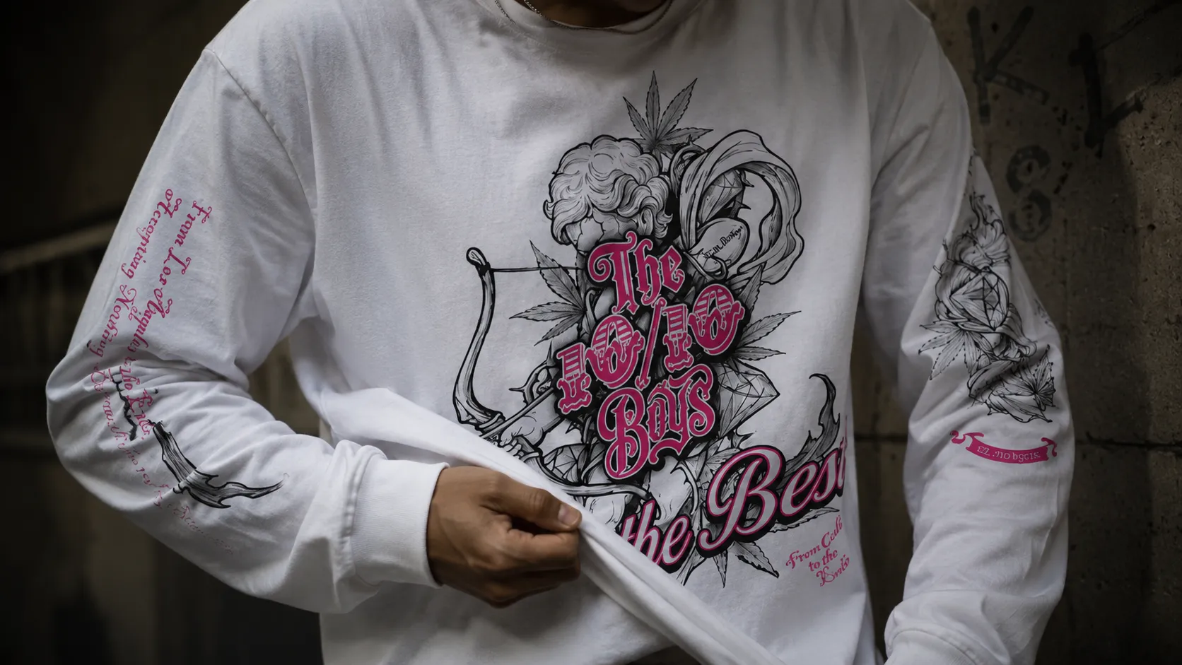 Close-up of a white long sleeve tee worn on the street, showing chest illustration and pink sleeve lettering