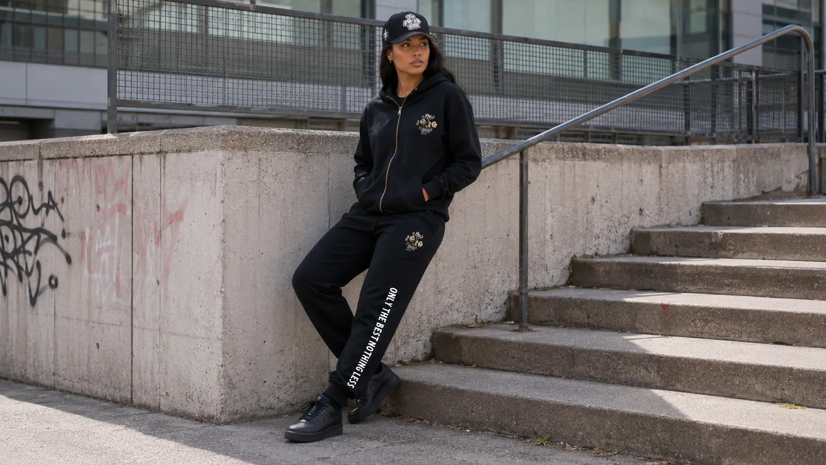 Hoodie and joggers outfit in all black, worn with a cap and low-profile trainers