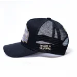The 10/10 Boys Trucker Hat in black — side profile showing the badge patch and mesh back panel