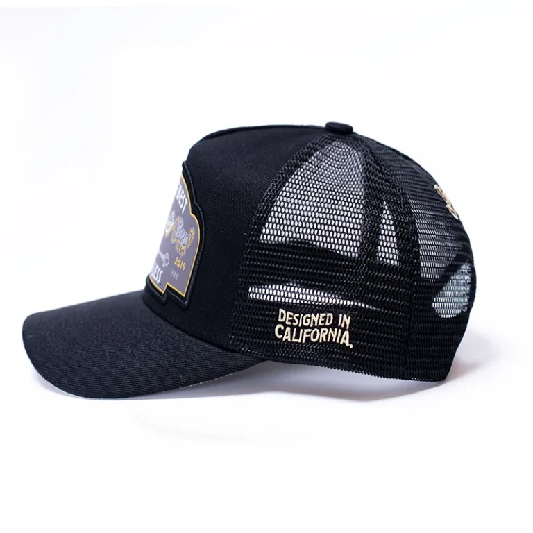 The 10/10 Boys Trucker Hat in black — side profile showing the badge patch and mesh back panel