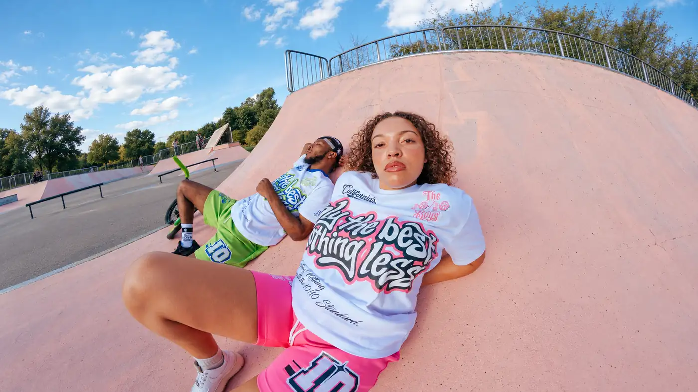 Two models lying on a skate ramp wearing California's Finest tees in green and pink up close